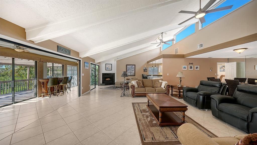 A spacious living room with vaulted ceilings, tile floors, a fireplace, and a sliding glass door — 3131 BAYOU SOUND, LONGBOAT KEY, FL