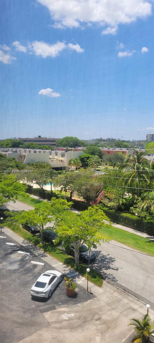 An elevated view shows a parking lot, green trees, and residential buildings under a blue sky — 1750 NE 115th St # 608, Miami FL 33181, MIAMI, FL