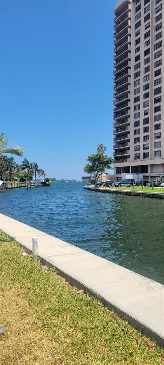 A tall apartment building stands beside a canal with a concrete seawall and grass — 1750 NE 115th St # 608, Miami FL 33181, MIAMI, FL
