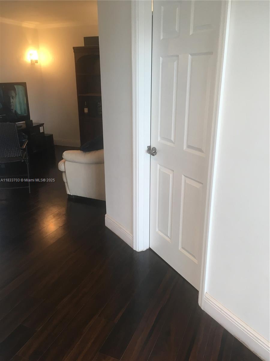 A white door stands next to a living area with dark wood floors and furniture — 1750 NE 115th St # 608, Miami FL 33181, MIAMI, FL