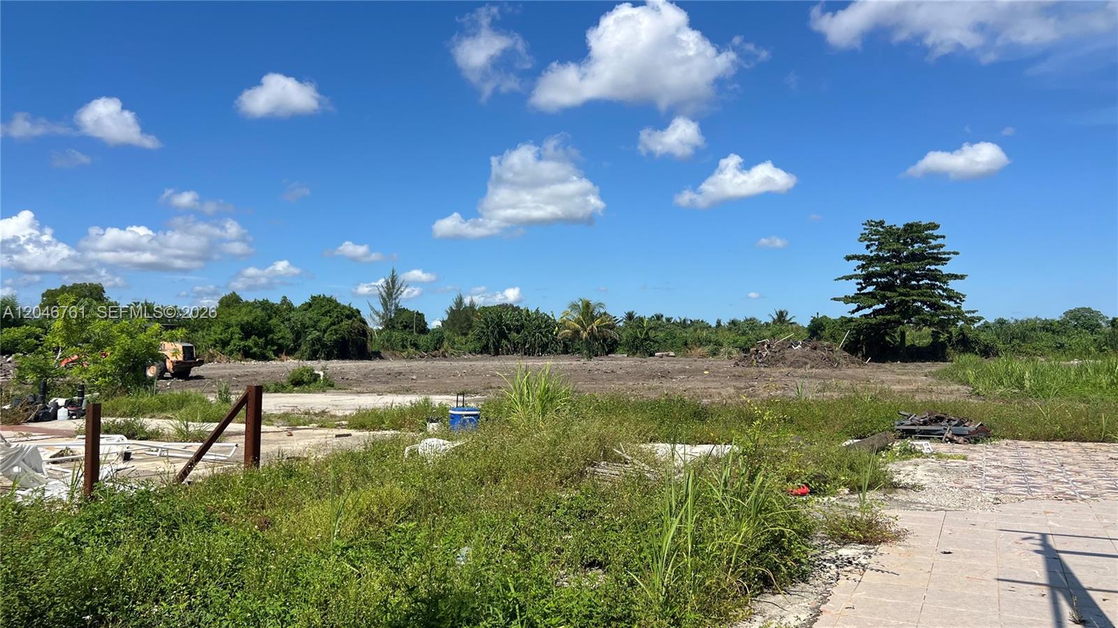 A vacant, cleared lot with overgrown grass and scattered debris under a blue sky — 15820 SW 209th Ave, Miami FL 33187, MIAMI, FL