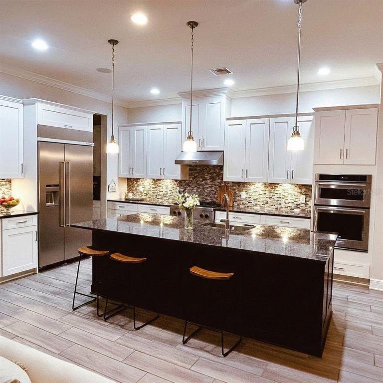 A kitchen features white cabinets, a dark island with bar stools, and stainless steel appliances — 3191 PLAYERS VIEW CIRCLE, LONGWOOD, FL