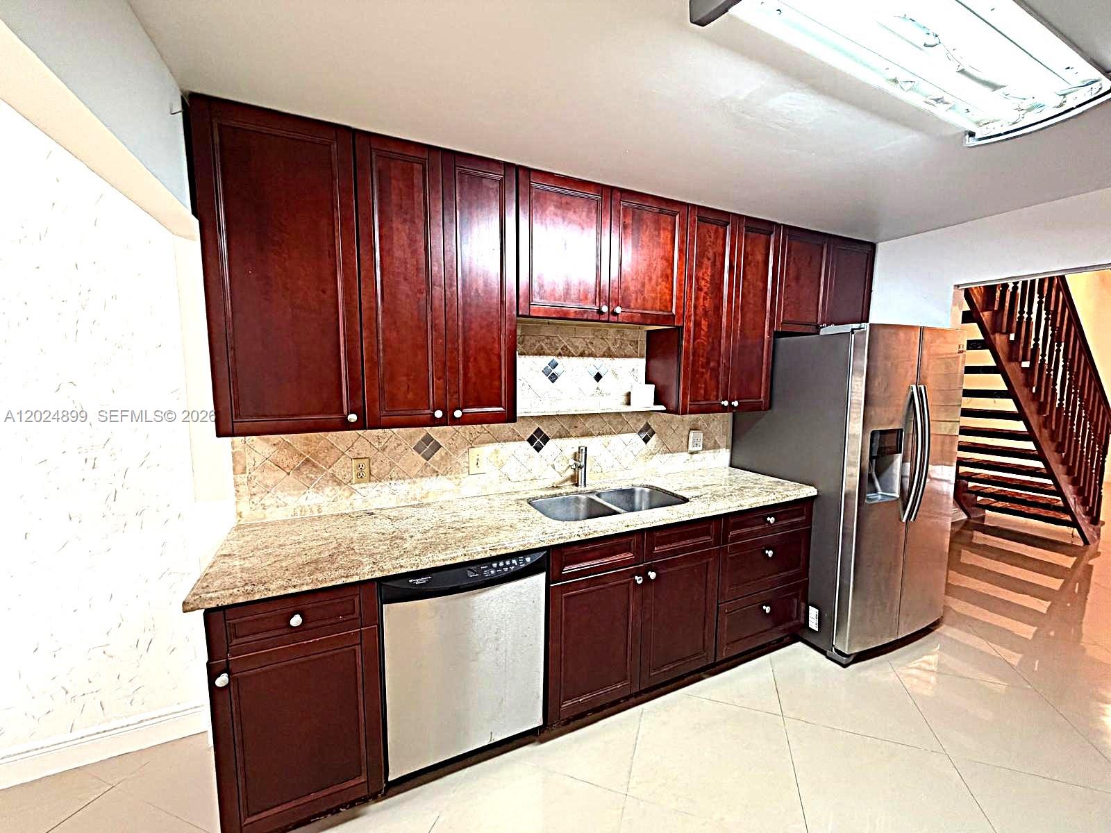 A kitchen features dark wood cabinets, granite countertops, stainless steel appliances, and a staircase nearby — 6620 Tiburon Cir # 3, Boca Raton FL 33433, BOCA RATON, FL