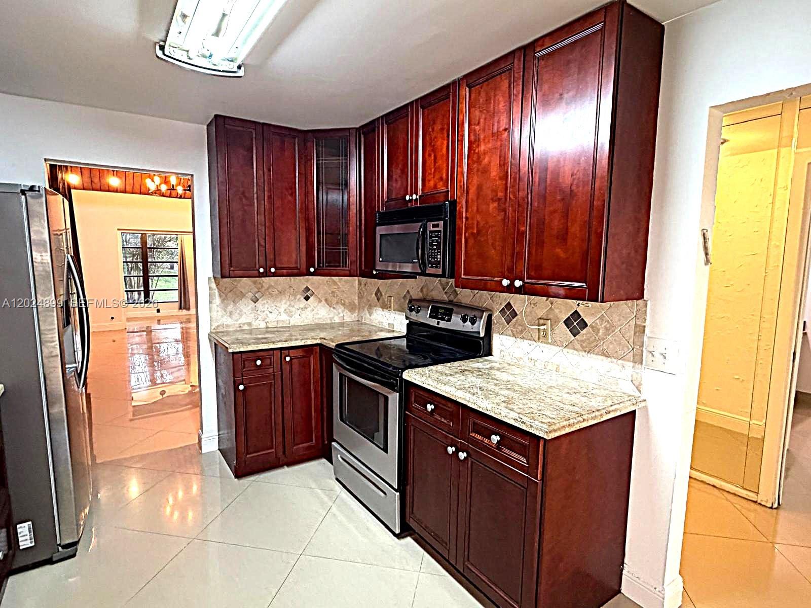 A kitchen features dark wood cabinets, granite countertops, stainless steel appliances, and tiled flooring — 6620 Tiburon Cir # 3, Boca Raton FL 33433, BOCA RATON, FL