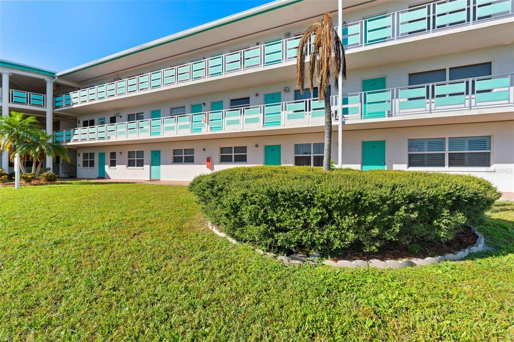 Exterior view of a multi-story apartment building with teal doors and white railings — 1950 59TH AVENUE N UNIT 114, ST PETERSBURG, FL