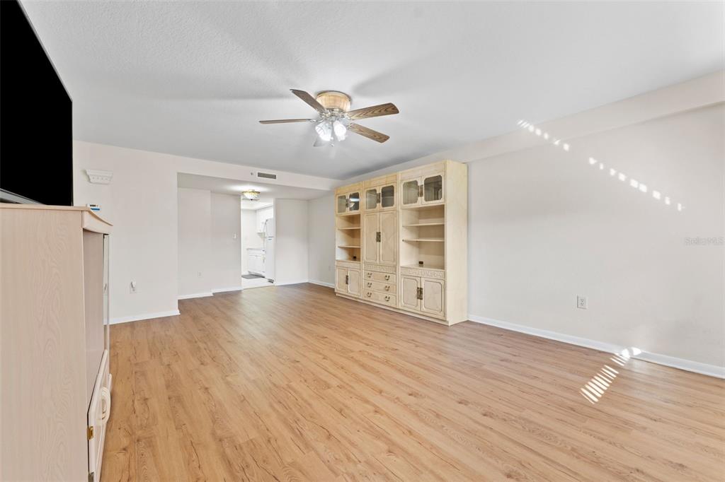 A living room with wood-look flooring, a ceiling fan, and a large built-in wall unit — 1950 59TH AVENUE N UNIT 114, ST PETERSBURG, FL