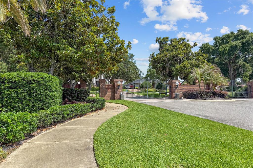 A paved walkway leads toward a gated brick entrance surrounded by trees and landscaping — Lot 47 OSPREY POINTE BOULEVARD, CLERMONT, FL