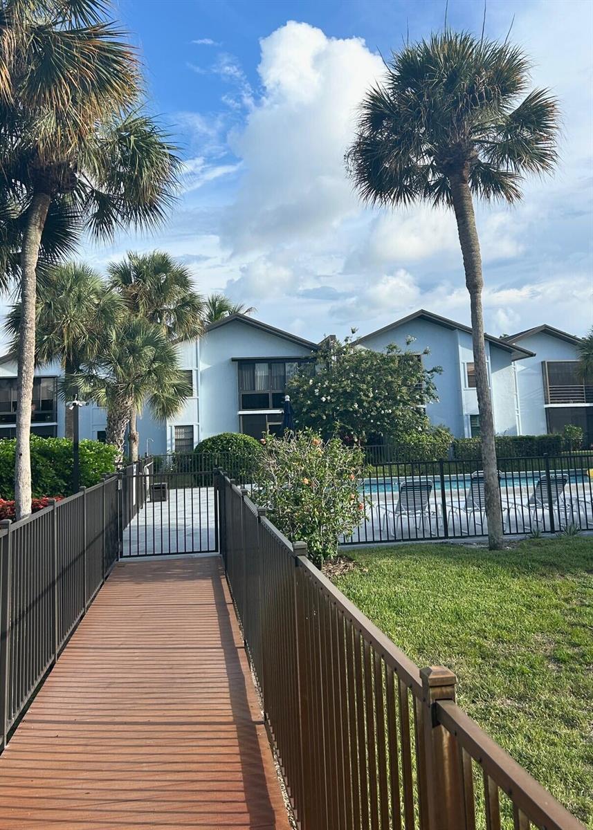 A wooden walkway leads to a gated swimming pool area surrounded by palm trees — 1811 SW Palm City Road # A602, Stuart FL 34994, STUART, FL