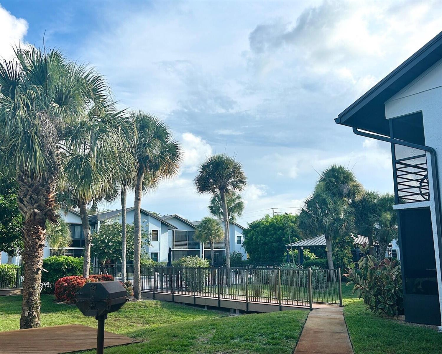Exterior view of a residential complex with palm trees, a footbridge, and a grassy lawn — 1811 SW Palm City Road # A602, Stuart FL 34994, STUART, FL