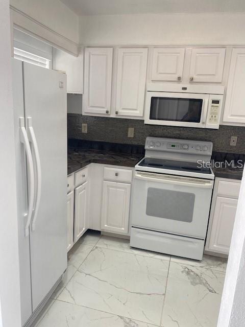 A kitchen with white cabinets, white appliances, dark countertops, and light-colored marble-patterned tile flooring — 1820 AMBERLY AVENUE UNIT T10, ORLANDO, FL