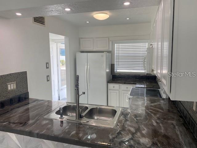 A kitchen features white cabinets, a dark marbled countertop, a double sink, and a refrigerator — 1820 AMBERLY AVENUE UNIT T10, ORLANDO, FL