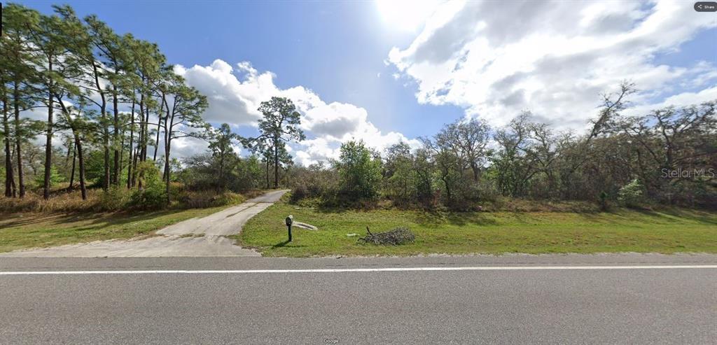 A paved driveway leads from a road into a wooded, undeveloped lot with scattered trees — COMMONWEALTH AVE N, POLK CITY, FL