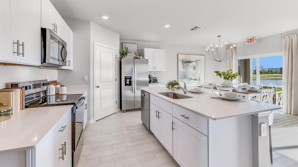 A modern kitchen features white cabinets, stainless steel appliances, a large island, and dining area — 1445 MABLETON DRIVE, PORT CHARLOTTE, FL