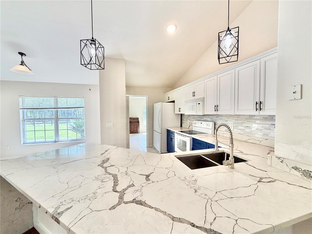A kitchen features white cabinets, blue lower cabinets, and a large marble-patterned island countertop — 12748 NW 148TH TERRACE, ALACHUA, FL
