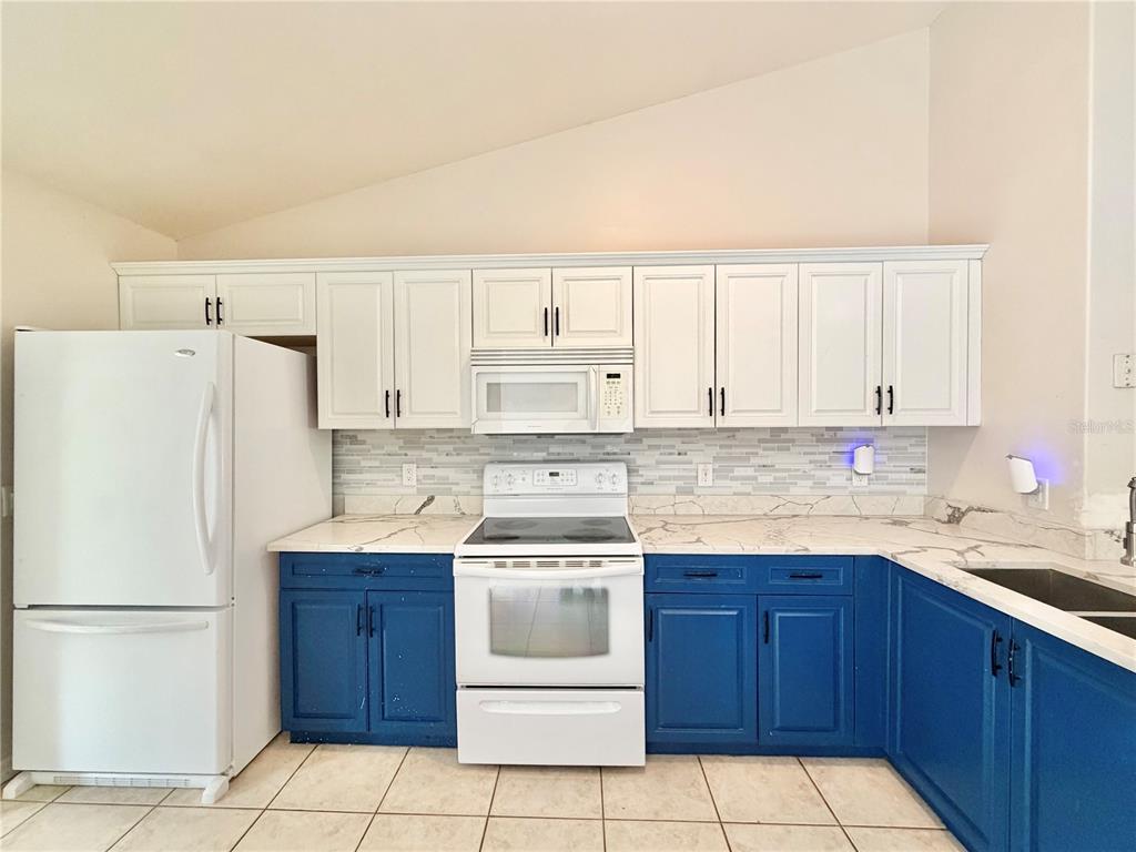 A kitchen features white upper cabinets, blue lower cabinets, white appliances, and marble-look countertops — 12748 NW 148TH TERRACE, ALACHUA, FL