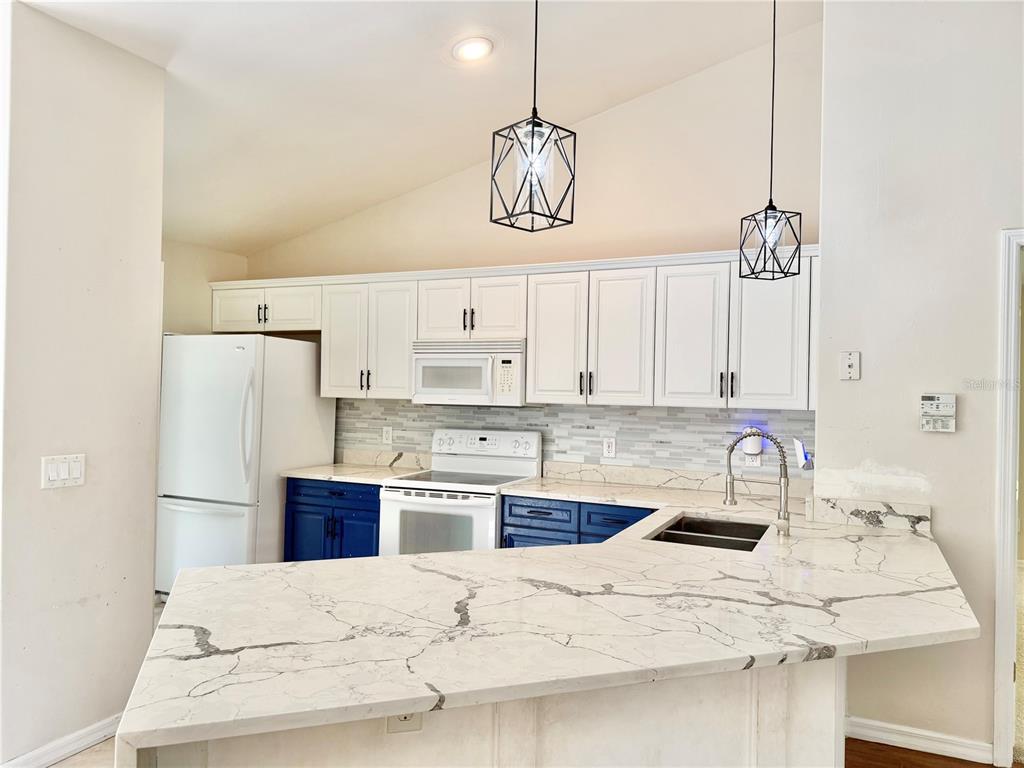 A kitchen features white upper cabinets, blue lower cabinets, white countertops, and two geometric pendant lights — 12748 NW 148TH TERRACE, ALACHUA, FL