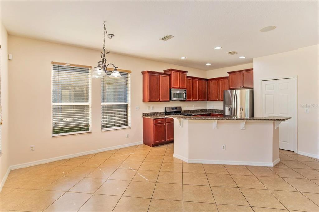 A kitchen with dark wood cabinets, granite countertops, and tile flooring features an attached breakfast bar — 14543 WHITTRIDGE DRIVE, WINTER GARDEN, FL