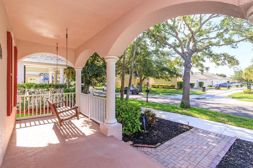 A covered porch features a hanging wooden swing, white railings, and arched architectural columns — 14543 WHITTRIDGE DRIVE, WINTER GARDEN, FL