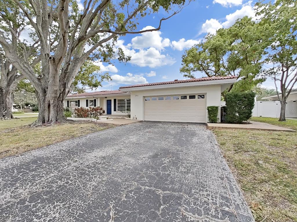 A single-story house with a white exterior, a two-car garage, and a cracked asphalt driveway — 1701 LAURIE LANE, BELLEAIR, FL