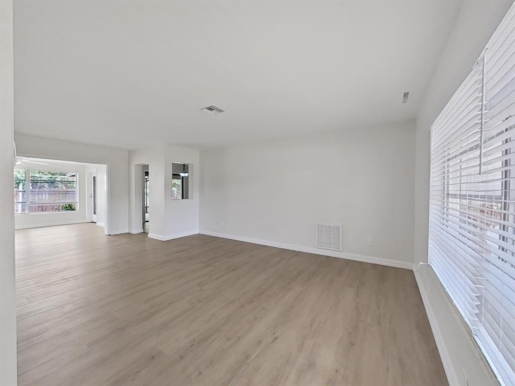 An empty living room features light wood-look flooring, white walls, and a large window — 1701 LAURIE LANE, BELLEAIR, FL