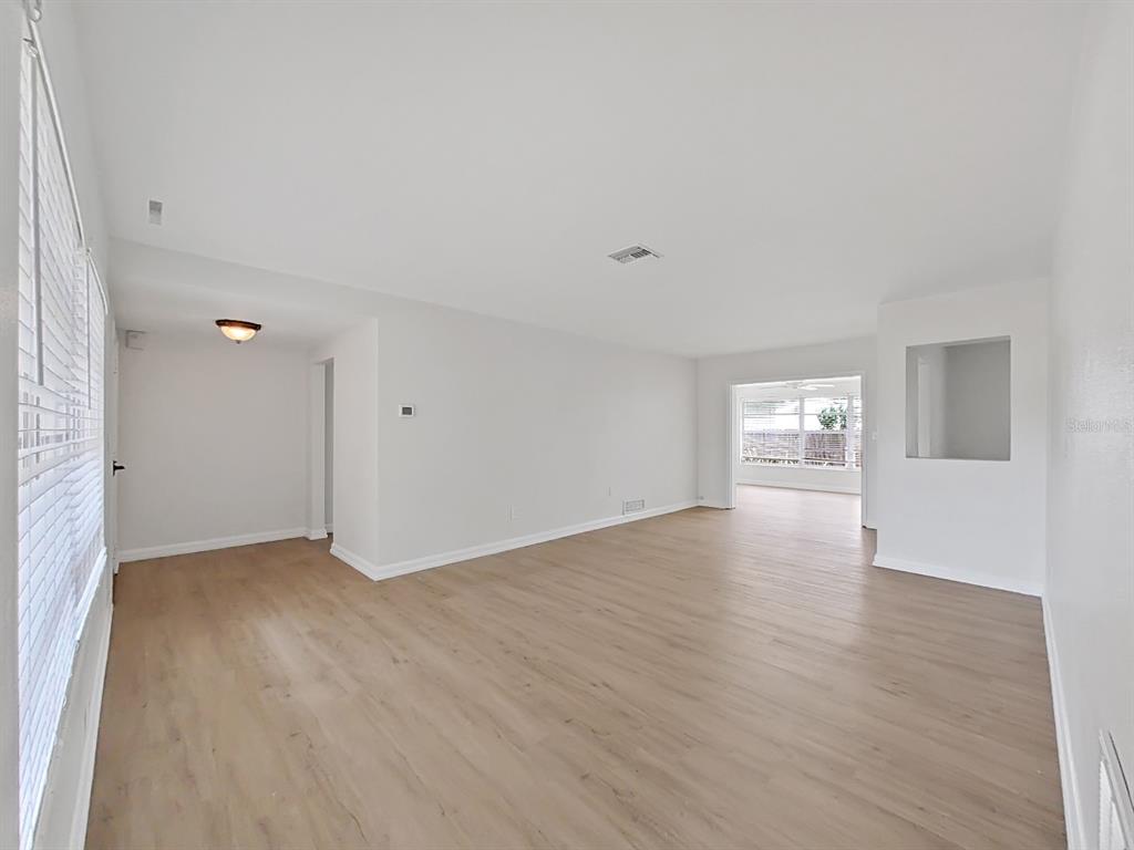 A bright, empty living room features light wood-look flooring, white walls, and a large window — 1701 LAURIE LANE, BELLEAIR, FL