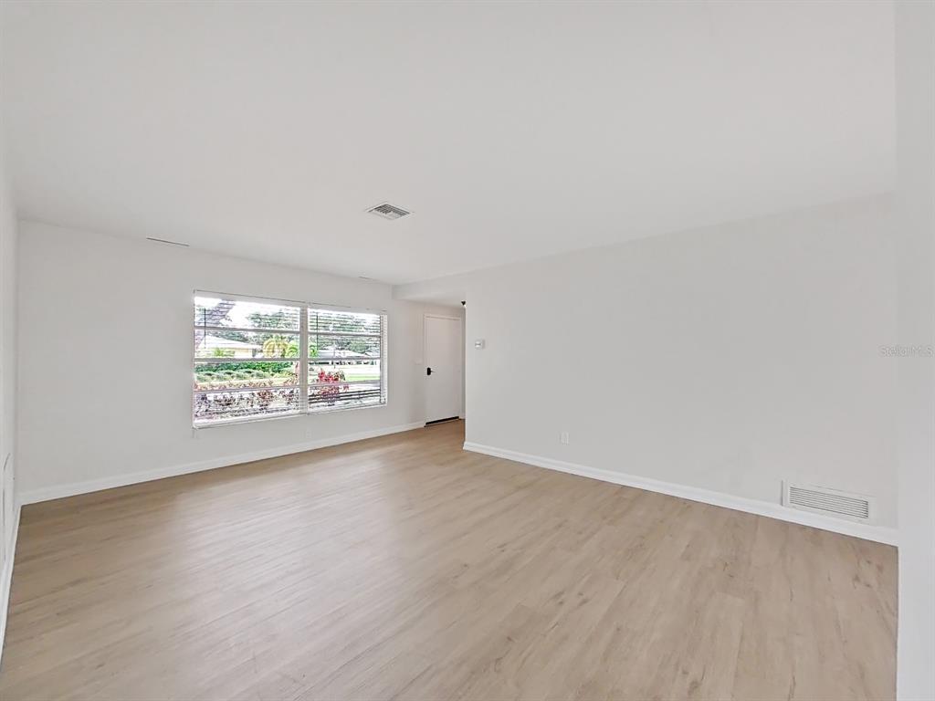 An empty room with light wood-look flooring, white walls, and a large window — 1701 LAURIE LANE, BELLEAIR, FL