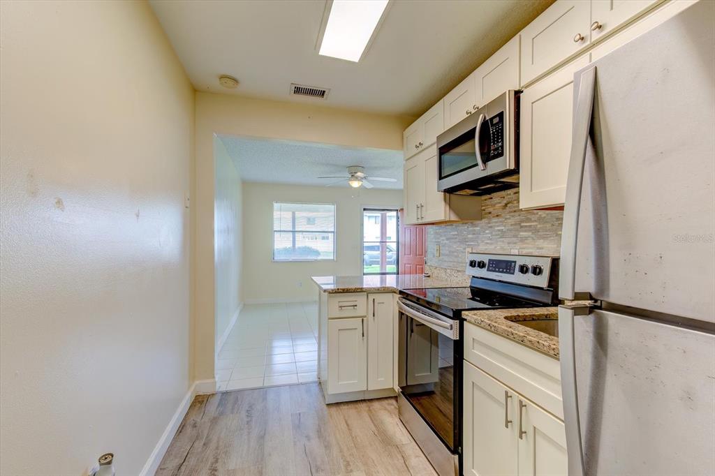 A kitchen with white cabinets, stainless steel appliances, and wood-look flooring leads to a dining area — 232 NORTHSHORE DRIVE UNIT A, ORMOND BEACH, FL