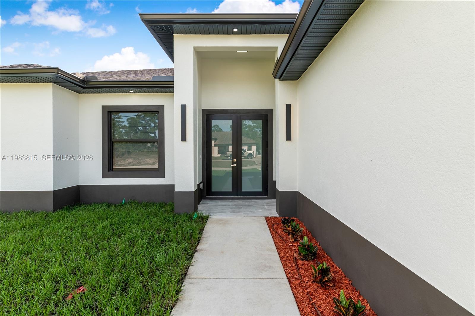 A modern, single-story white house with a dark garage door and a concrete driveway — 606 Johns Ave, Lehigh Acres FL 33972, LEHIGH ACRES, FL