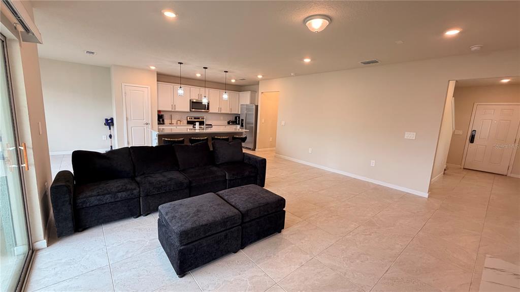 An open-concept living room features a black sectional sofa, tiled floors, and a kitchen island — 1347 RED BLOSSOM LANE, KISSIMMEE, FL