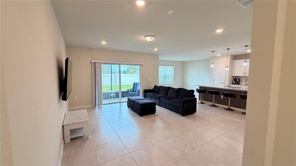 An open-concept living room features tile flooring, a dark sectional sofa, and a kitchen island — 1347 RED BLOSSOM LANE, KISSIMMEE, FL