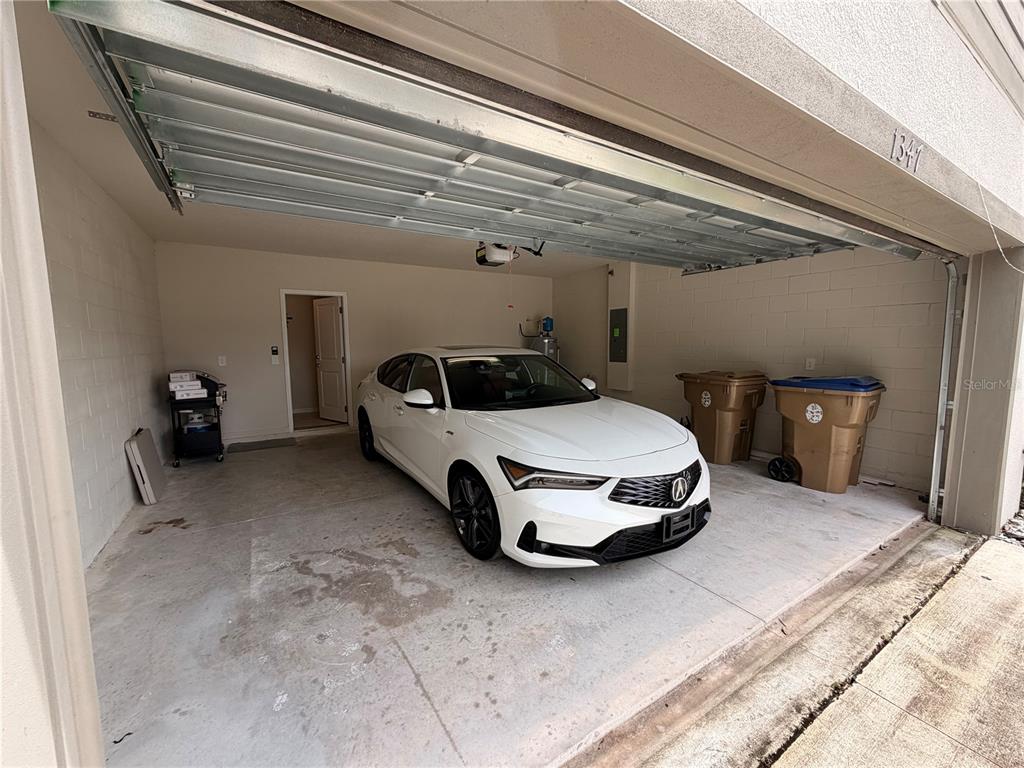 A white sedan is parked inside a garage with concrete block walls and two trash bins — 1347 RED BLOSSOM LANE, KISSIMMEE, FL