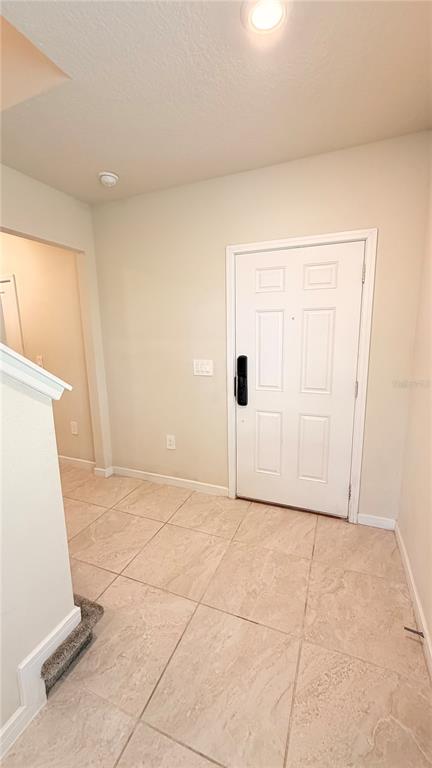An entryway features light-colored tile flooring, a white front door, and a staircase railing — 1347 RED BLOSSOM LANE, KISSIMMEE, FL
