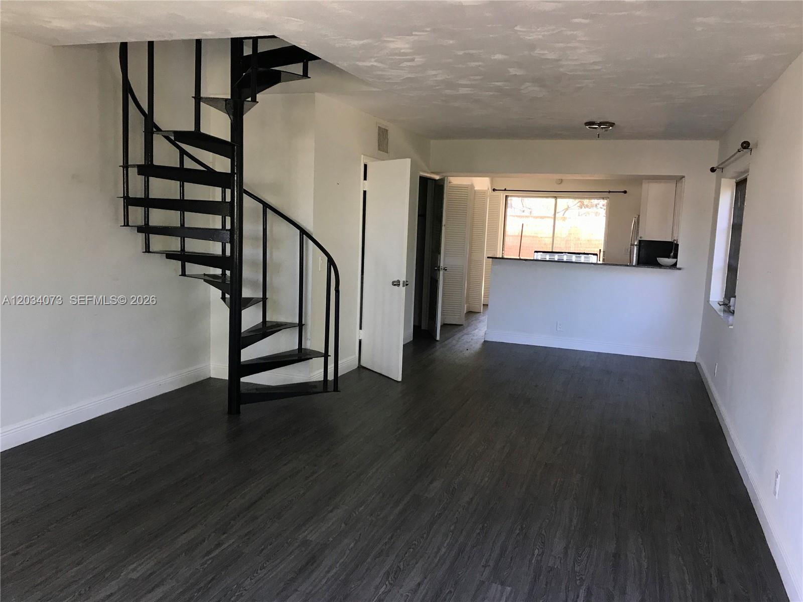 An open living area features dark wood-look flooring, a black spiral staircase, and a kitchen — 2444 SW 58 Mnr, Dania Beach FL 33312, DANIA BEACH, FL
