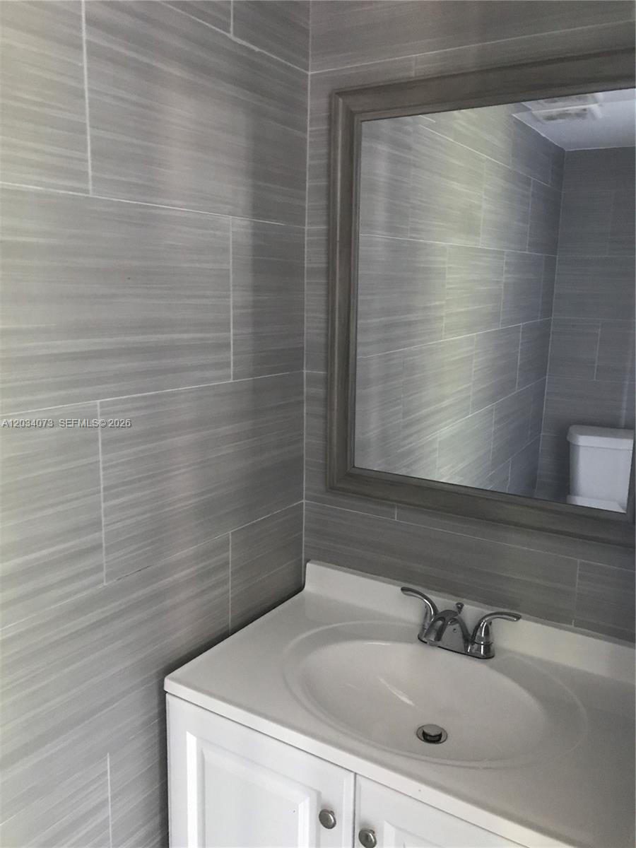 A bathroom features a white vanity, a framed mirror, and gray horizontal-patterned wall tiles — 2444 SW 58 Mnr, Dania Beach FL 33312, DANIA BEACH, FL