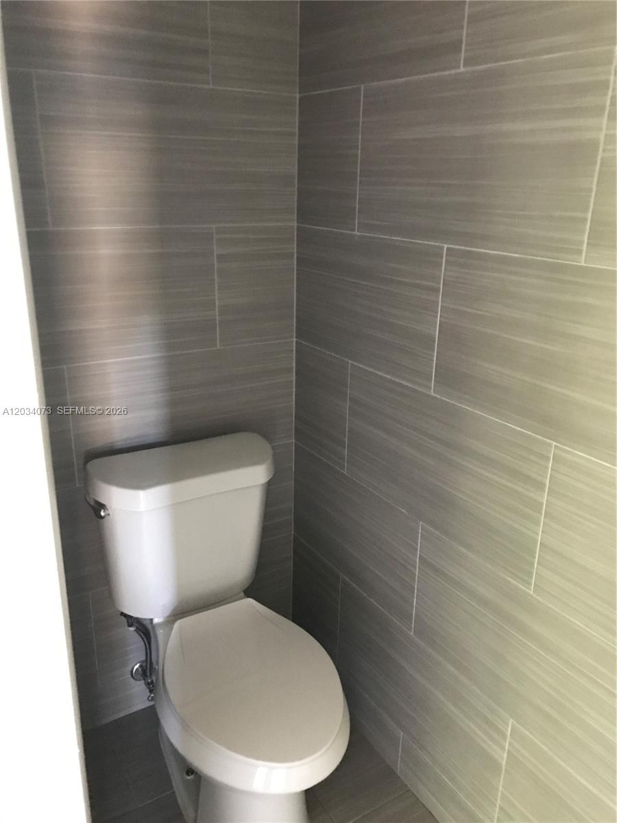 A toilet is positioned in a small corner tiled with horizontal gray rectangular tiles — 2444 SW 58 Mnr, Dania Beach FL 33312, DANIA BEACH, FL