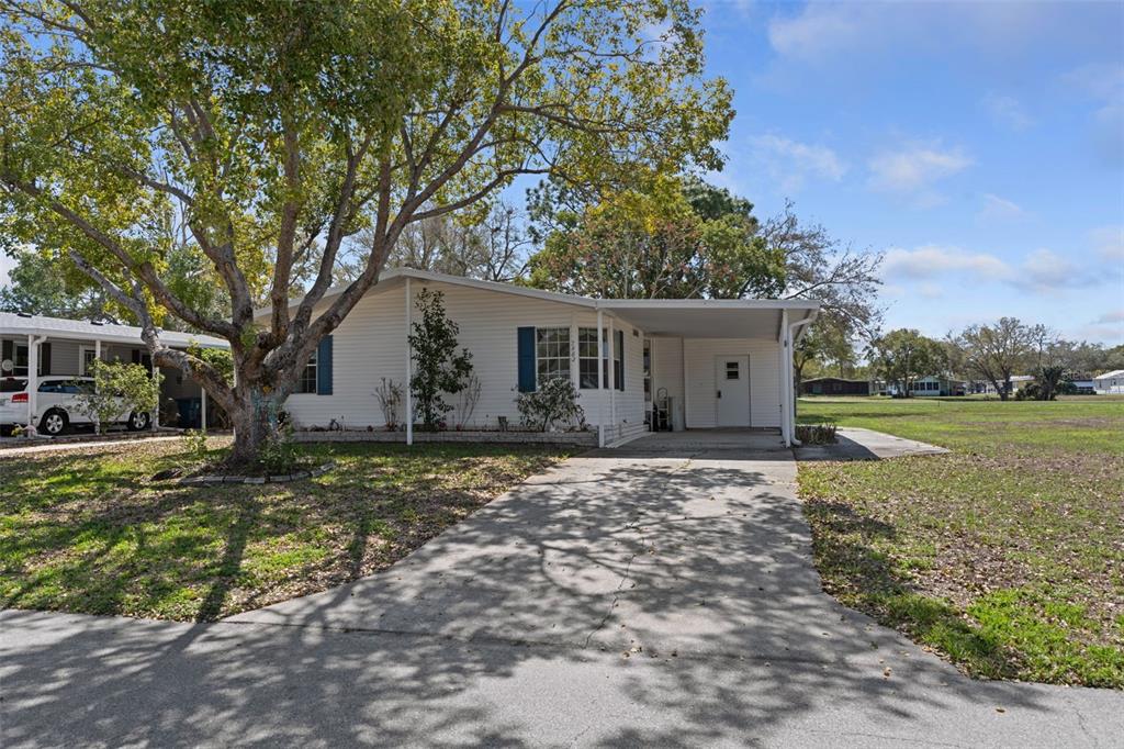 A white single-story manufactured home features a concrete driveway, a carport, and a large tree — 7482 DINSMORE STREET, BROOKSVILLE, FL