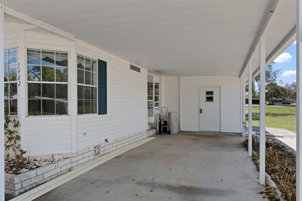 A covered concrete carport sits beside the white siding of a manufactured home — 7482 DINSMORE STREET, BROOKSVILLE, FL