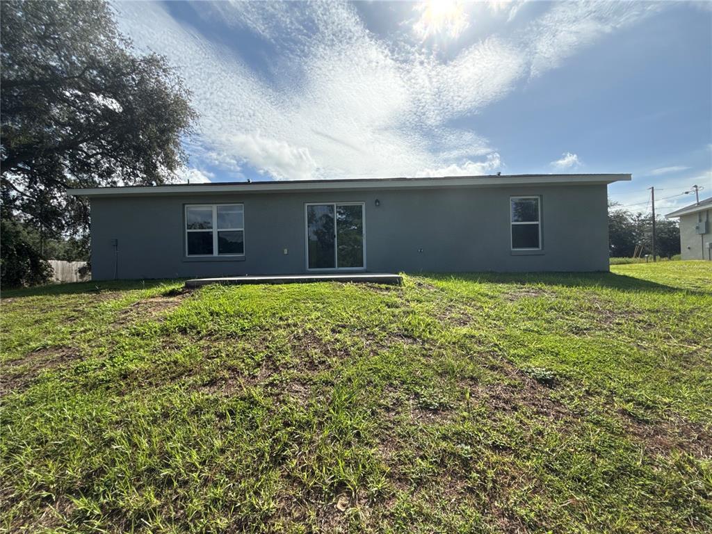 The rear exterior of a gray house features a sliding glass door and two windows — 22 MALAUKA CIRCLE, OCKLAWAHA, FL