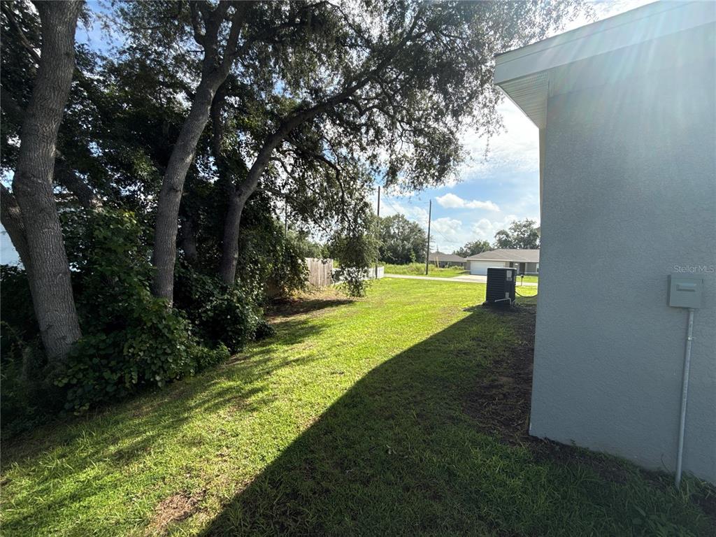 A grassy side yard with large trees sits beside the exterior wall of a house — 22 MALAUKA CIRCLE, OCKLAWAHA, FL
