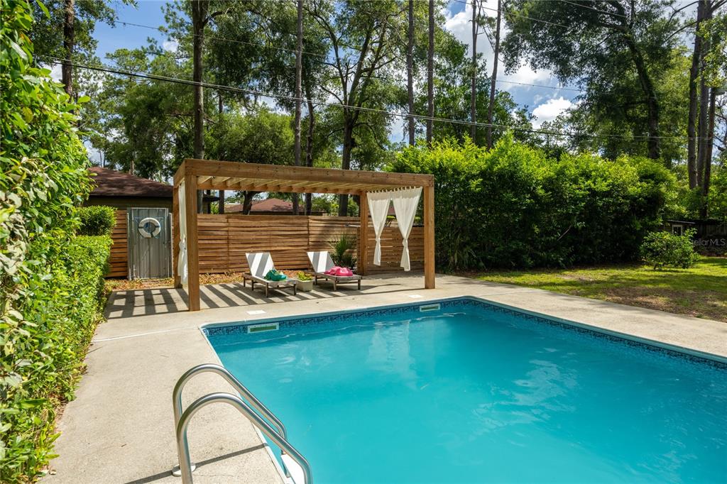 A backyard features a swimming pool with a metal ladder and a wooden pergola — 4204 NW 19TH PLACE, GAINESVILLE, FL