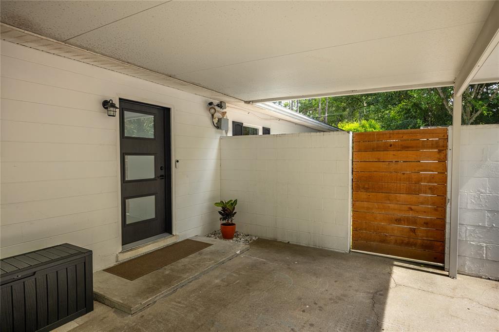 A covered carport features a dark front door, a concrete floor, and a wooden gate — 4204 NW 19TH PLACE, GAINESVILLE, FL