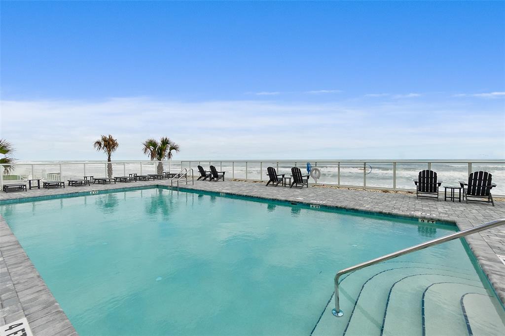 A rectangular swimming pool sits on a paved patio overlooking the ocean — 2055 S ATLANTIC AVENUE UNIT 1006, DAYTONA BEACH, FL