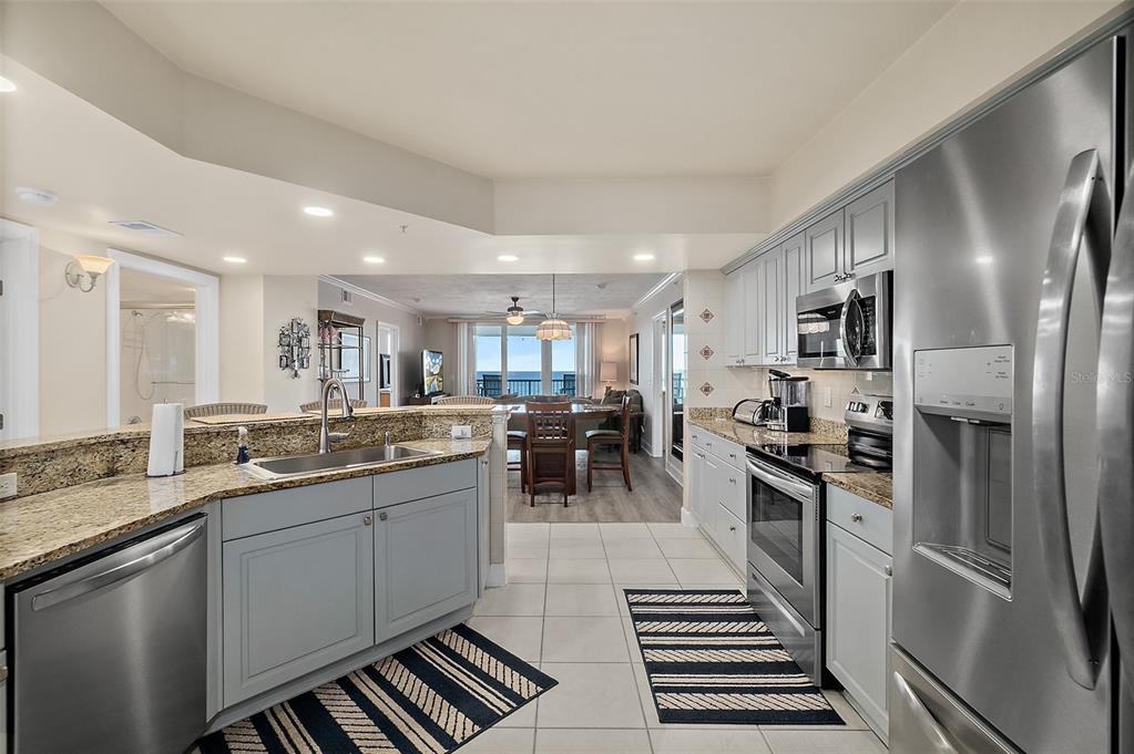 A kitchen with gray cabinets, granite countertops, and stainless steel appliances overlooks a dining area — 2055 S ATLANTIC AVENUE UNIT 1006, DAYTONA BEACH, FL