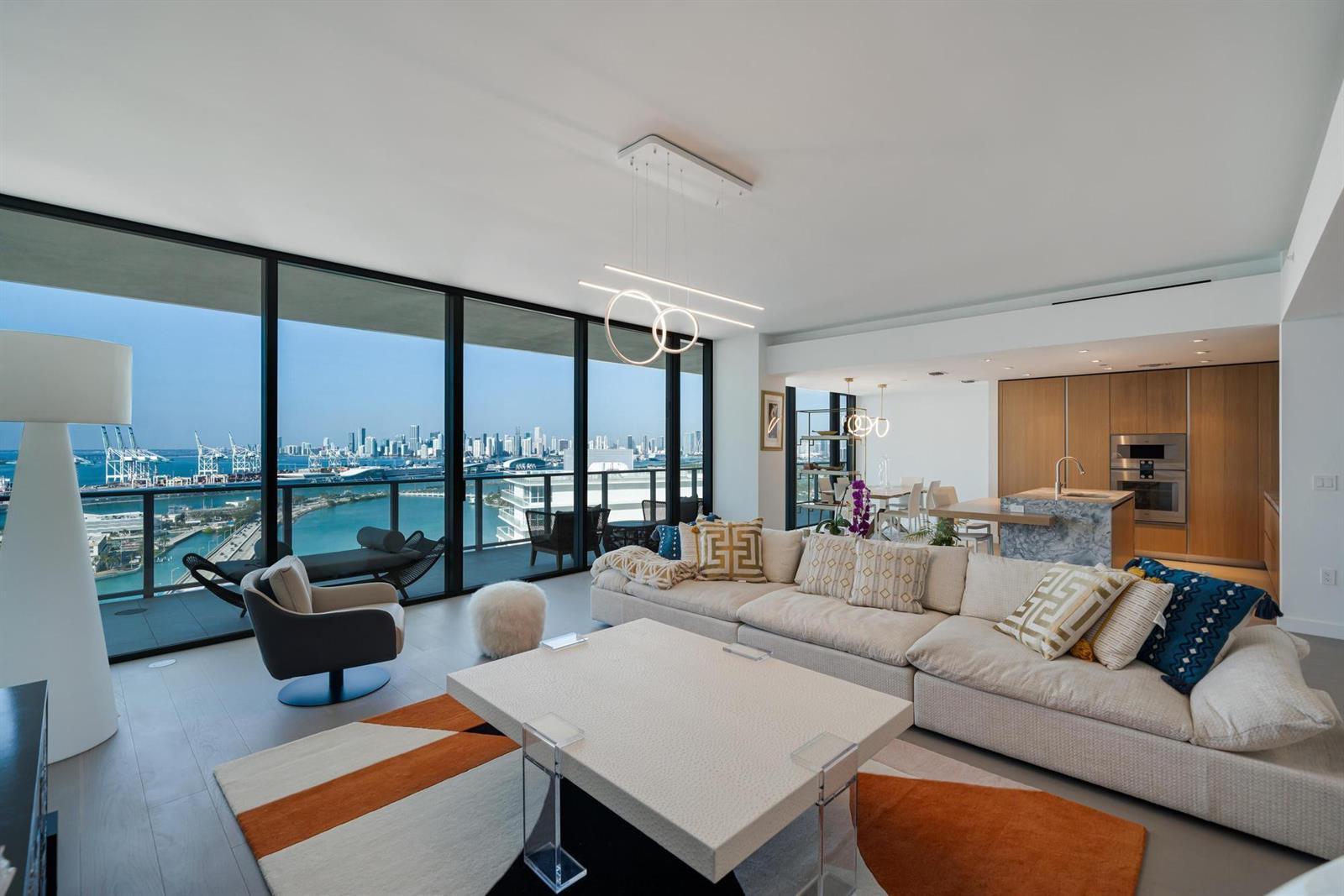 A modern living room features a large sectional sofa, a coffee table, and floor-to-ceiling windows — 500 Alton # 2702, Miami Beach FL 33139, MIAMI BEACH, FL