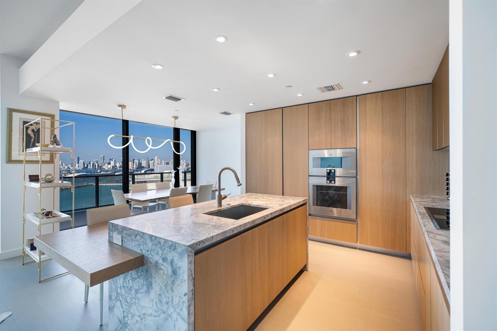 A modern kitchen features a marble-topped island, light wood cabinetry, and a city skyline view — 500 Alton # 2702, Miami Beach FL 33139, MIAMI BEACH, FL