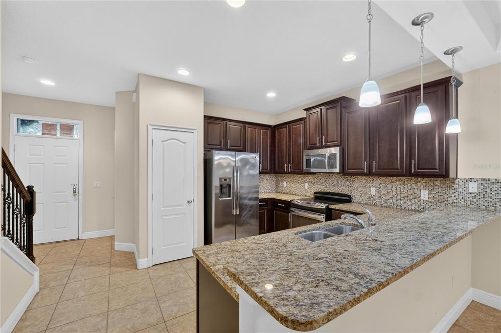 A kitchen features dark wood cabinets, granite countertops, stainless steel appliances, and a tile floor — 8087 BROOKSVILLE DRIVE, DAVENPORT, FL
