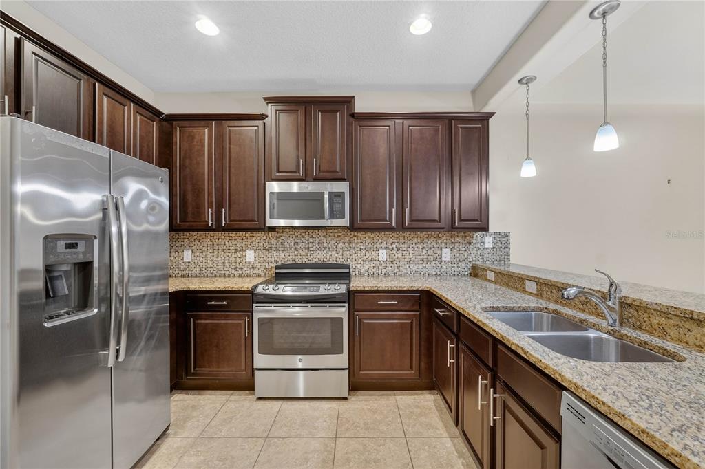 A kitchen features dark wood cabinets, granite countertops, stainless steel appliances, and a tiled backsplash — 8087 BROOKSVILLE DRIVE, DAVENPORT, FL