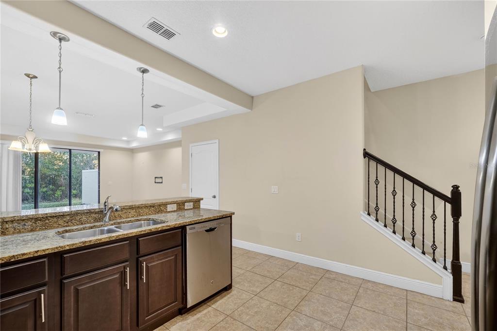 A kitchen with dark cabinets, granite countertops, and a staircase with a dark metal railing — 8087 BROOKSVILLE DRIVE, DAVENPORT, FL