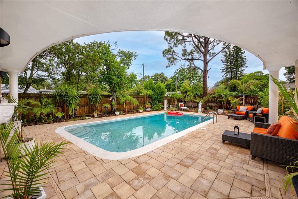 A rectangular swimming pool sits on a paved patio beneath a large covered arched porch — 755 43RD STREET N, ST PETERSBURG, FL