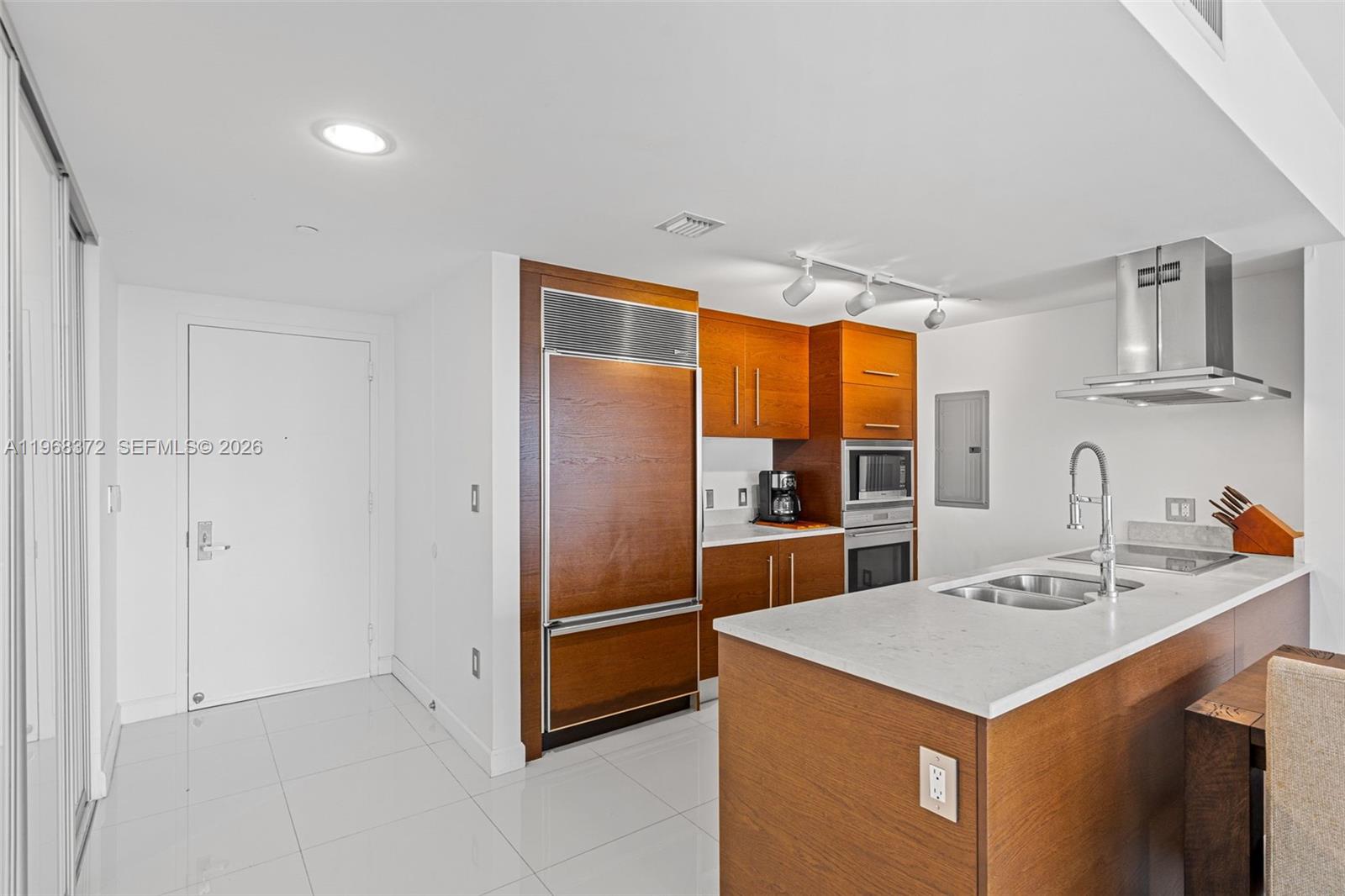 A modern kitchen features wood cabinetry, white countertops, stainless steel appliances, and white tile flooring — 495 Brickell Ave # 905, Miami FL 33131, MIAMI, FL